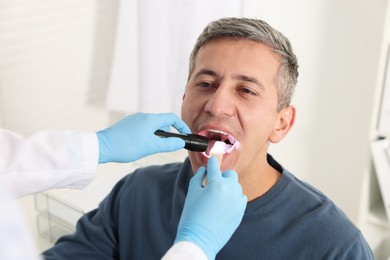 Doctor examining man's throat with flashlight in clinic