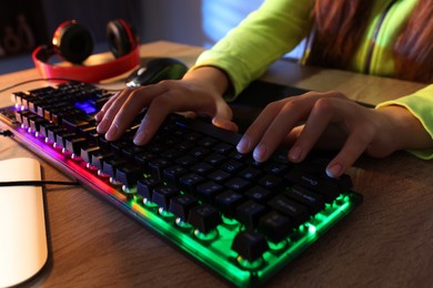 Girl using computer keyboard at wooden table indoors, closeup