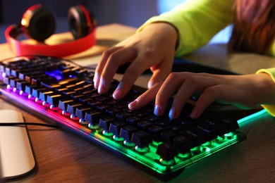 Girl using computer keyboard at wooden table indoors, closeup