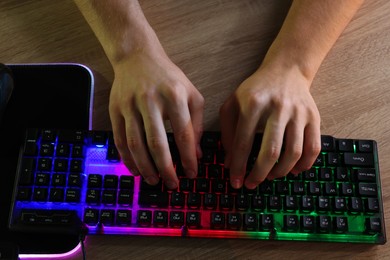 Photo of Young man using computer keyboard at wooden table indoors, closeup