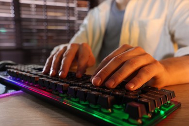 Young man using computer keyboard at wooden table indoors, closeup