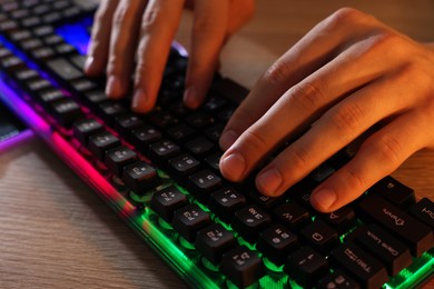 Young man using computer keyboard at wooden table indoors, closeup