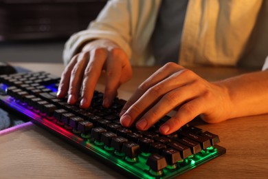 Young man using computer keyboard at wooden table indoors, closeup