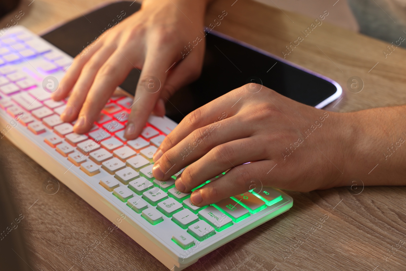 Photo of Young man using computer keyboard at wooden table indoors, closeup