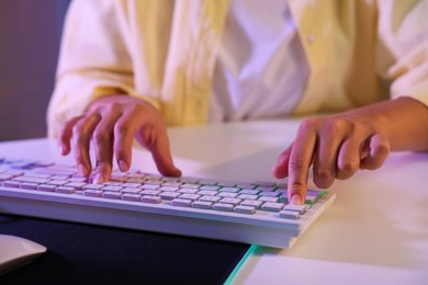 Photo of Woman using computer keyboard at white table indoors, closeup