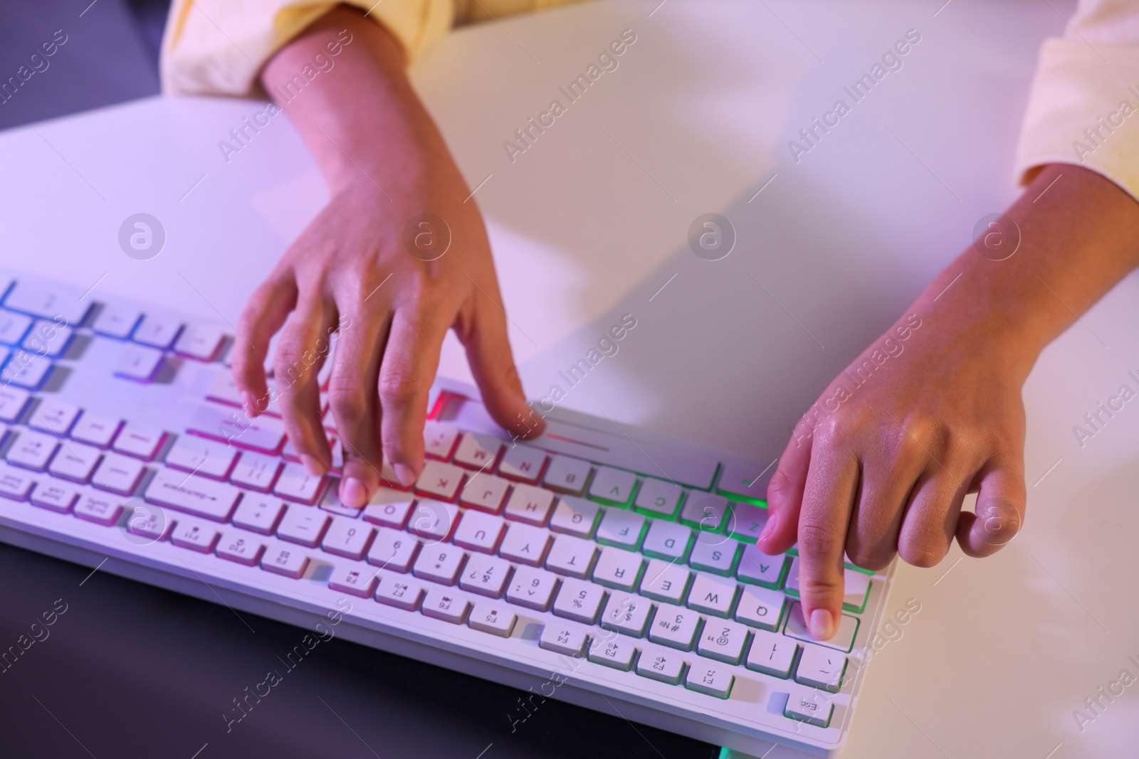 Photo of Woman using computer keyboard at white table indoors, closeup