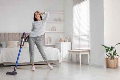 Young woman cleaning floor with cordless vacuum cleaner in bedroom