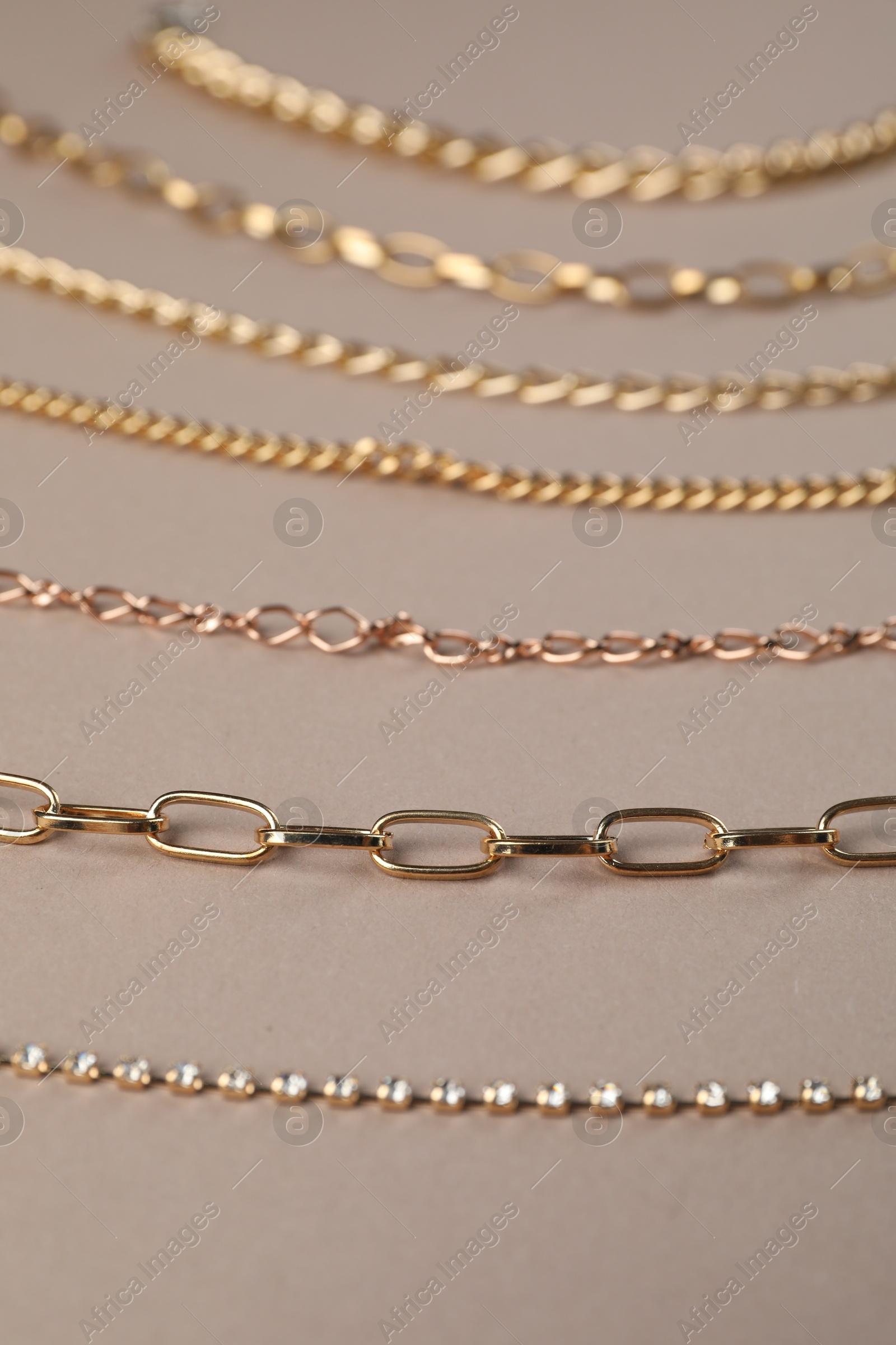 Photo of Different metal chains on light brown background, closeup. Luxury jewelry