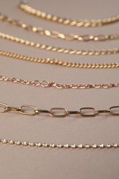 Photo of Different metal chains on light brown background, closeup. Luxury jewelry