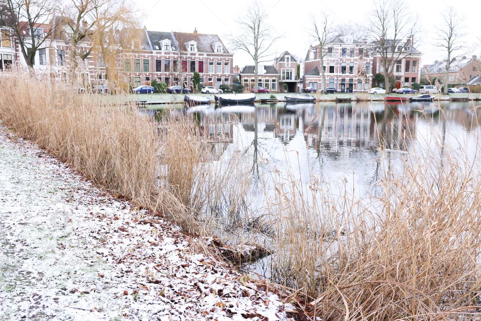 Photo of Picturesque view of water canal with moored boats, trees and buildings in city on winter day