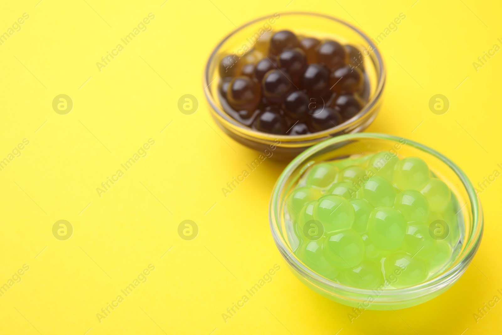 Photo of Color tapioca pearls in bowls on yellow background, closeup. Space for text