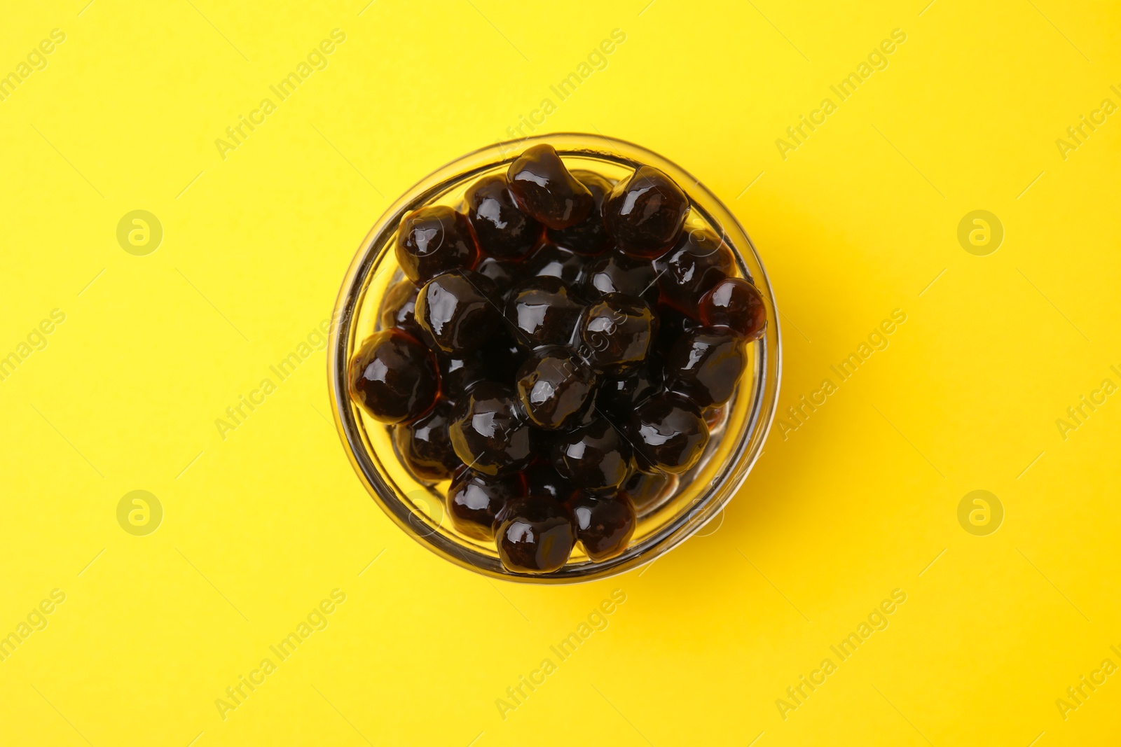 Photo of Dark tapioca pearls in bowl on yellow background, top view