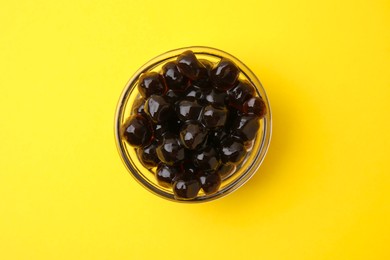 Photo of Dark tapioca pearls in bowl on yellow background, top view