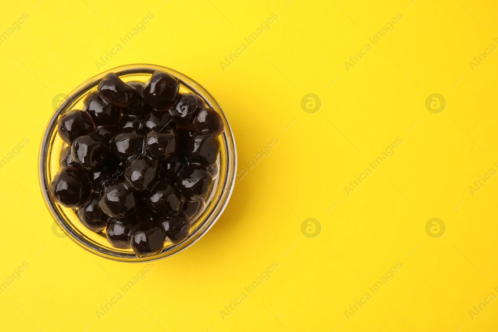 Photo of Dark tapioca pearls in bowl on yellow background, top view. Space for text