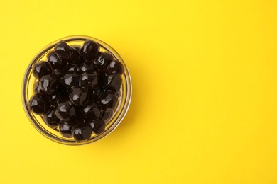 Photo of Dark tapioca pearls in bowl on yellow background, top view. Space for text