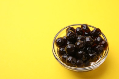 Photo of Dark tapioca pearls in bowl on yellow background, closeup. Space for text