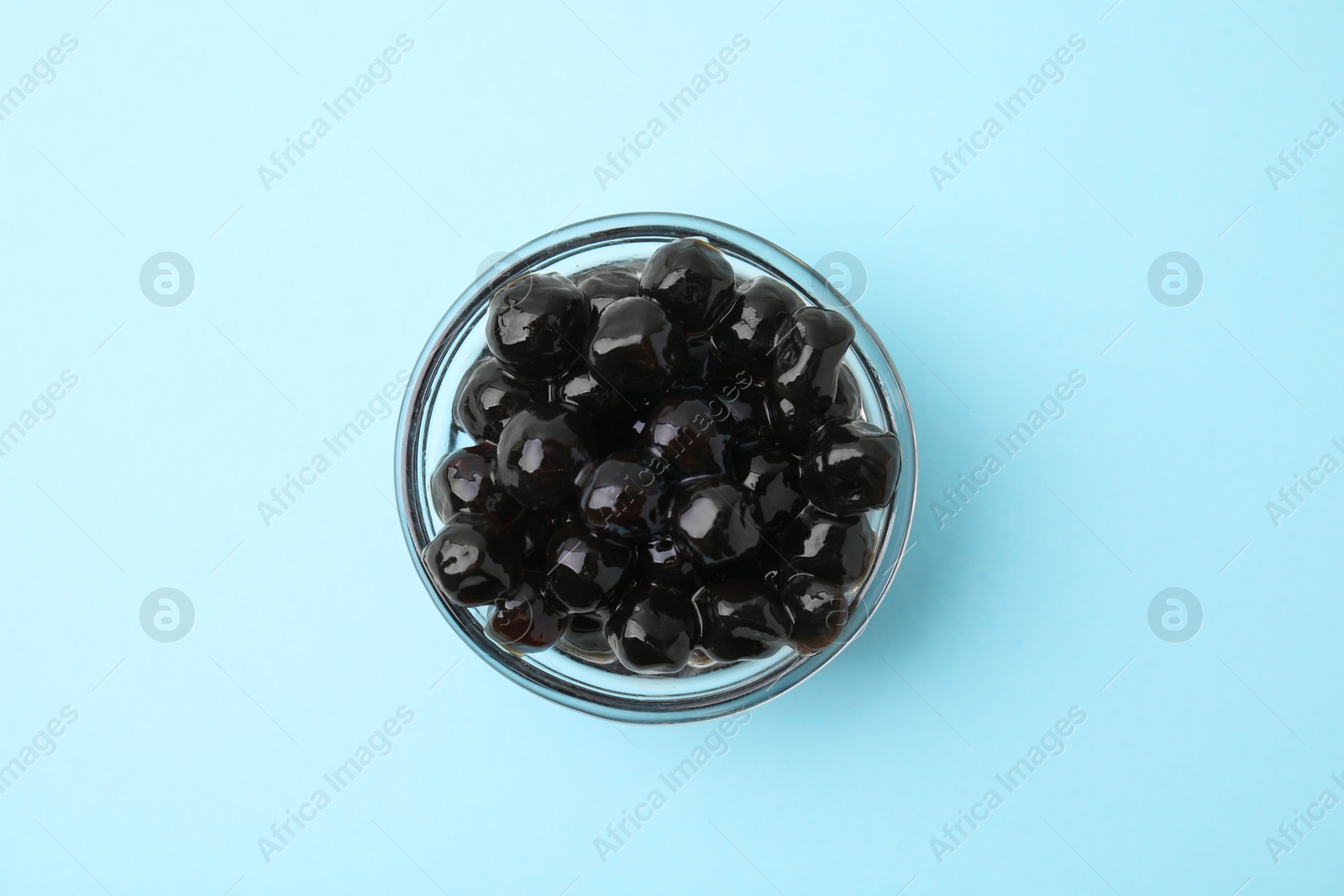 Photo of Dark tapioca pearls in bowl on light blue background, top view