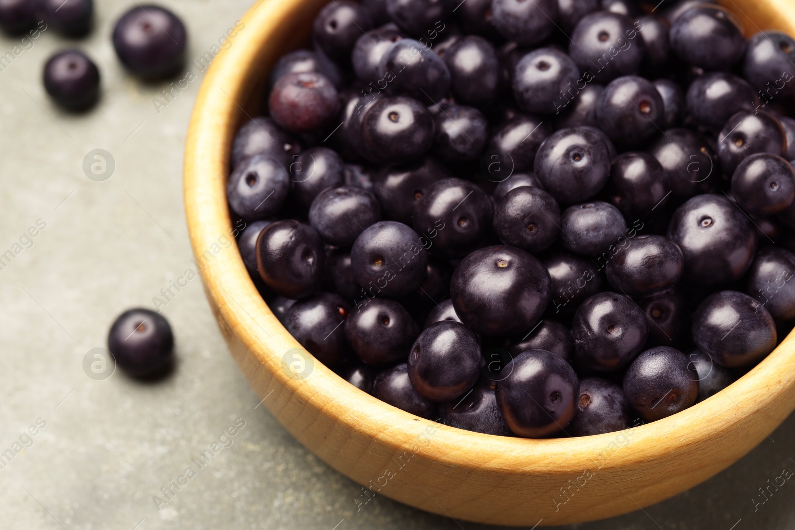 Photo of Ripe acai berries in bowl on grey textured table, closeup