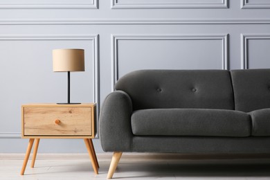 Photo of Stylish sofa and lamp on side table near grey wall