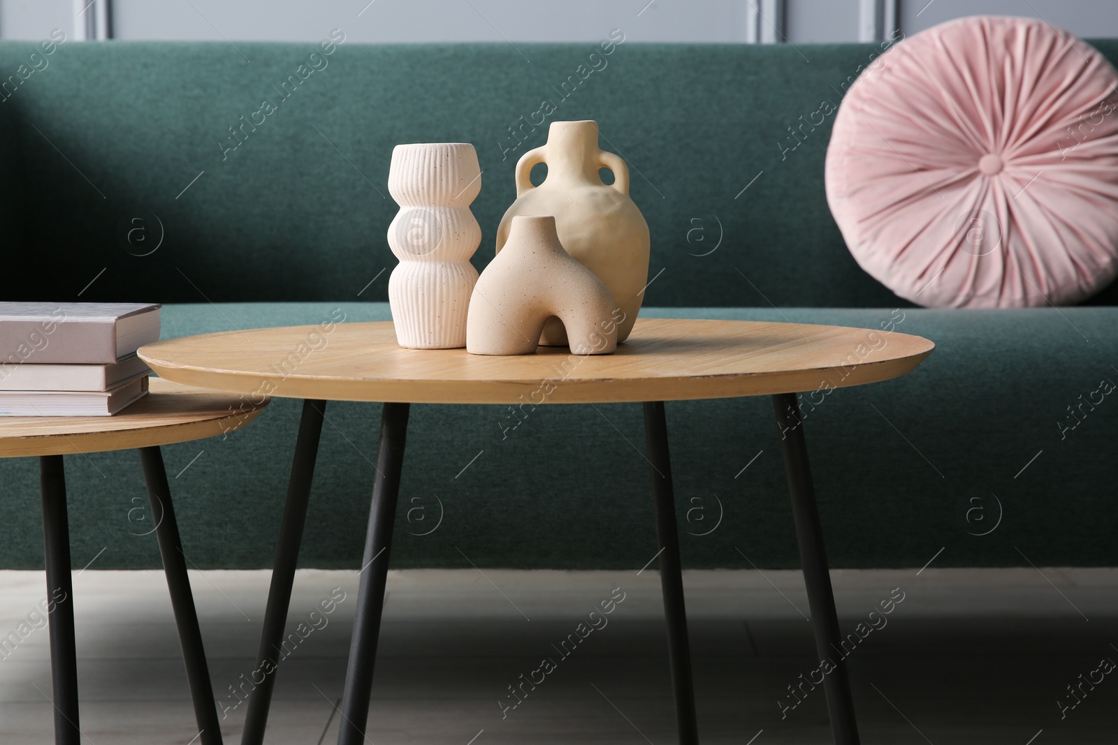 Photo of Stylish sofa with cushion, books and decor elements on nesting tables in room