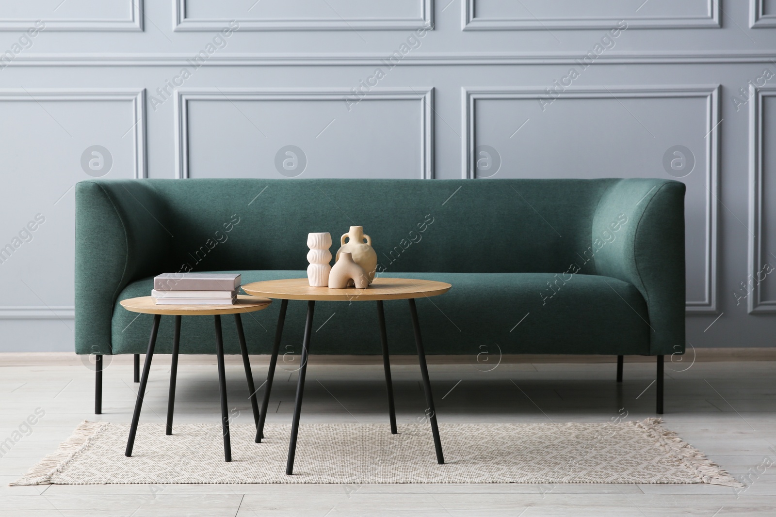 Photo of Stylish sofa, books and decor elements on nesting tables in room