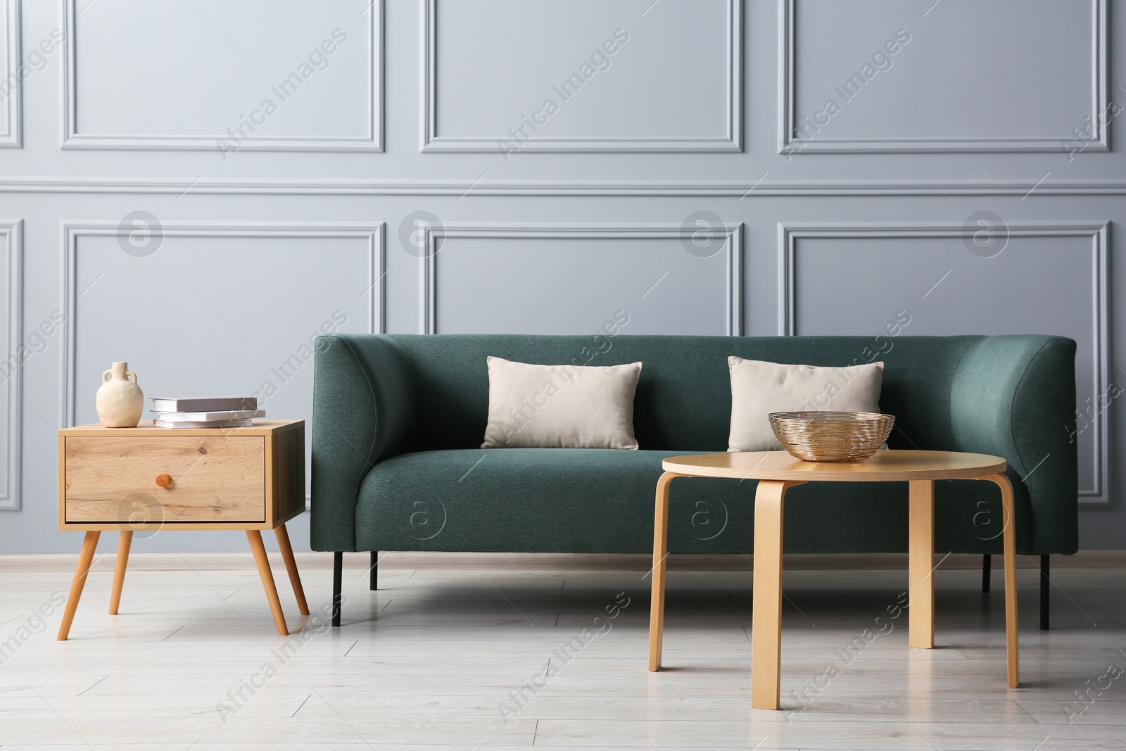 Photo of Stylish sofa with cushions, books and decor elements on side tables in room