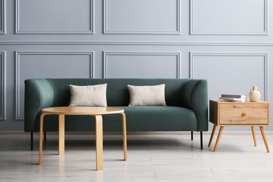 Photo of Stylish sofa with cushions and books on side table in room