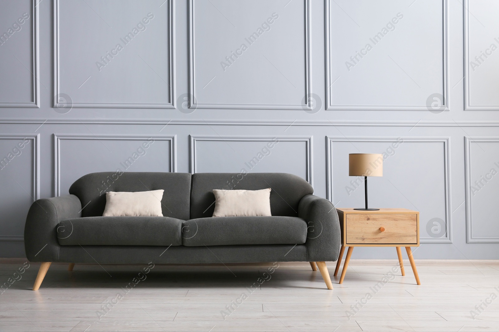 Photo of Stylish sofa with cushions and lamp on side table near grey wall