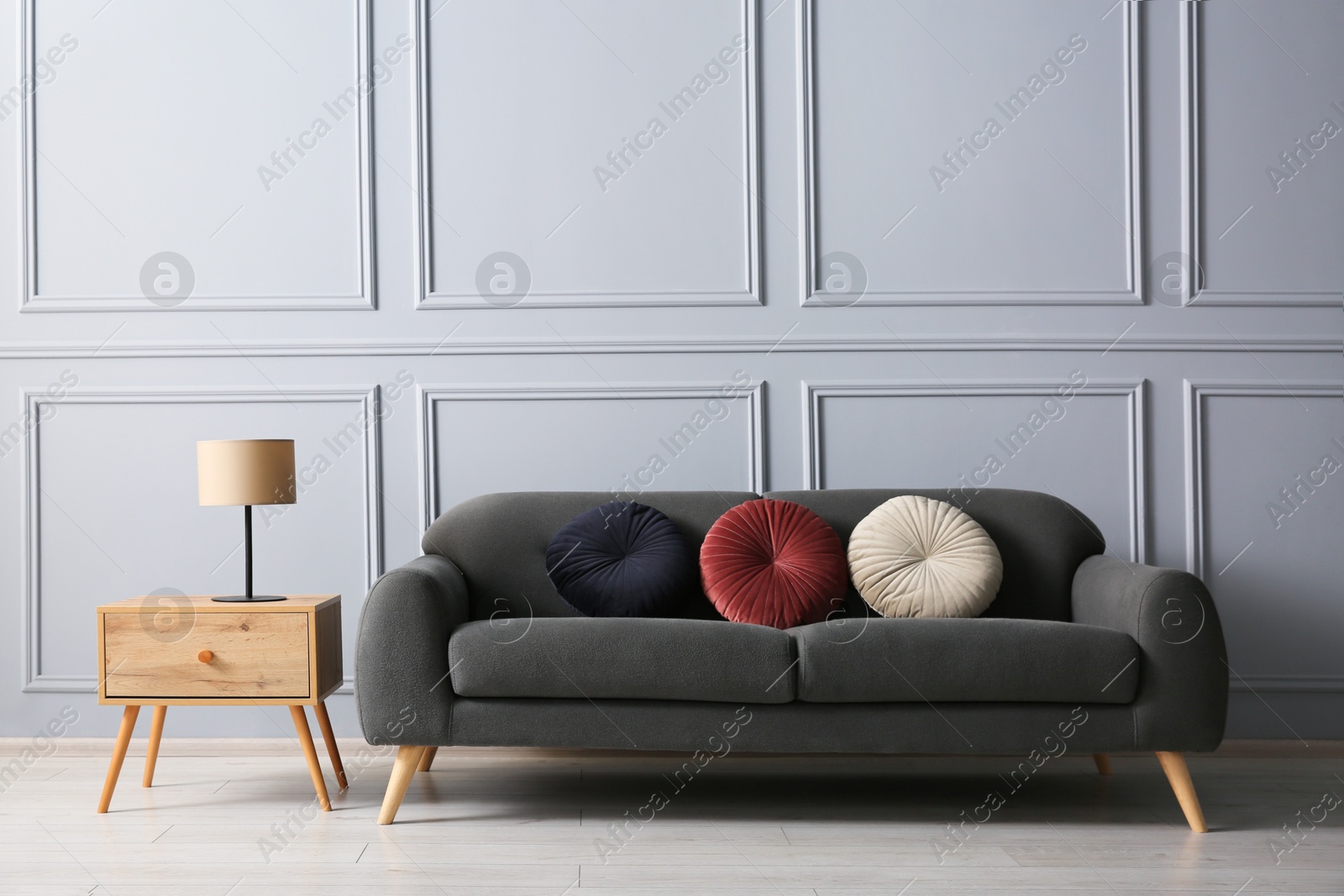 Photo of Stylish sofa with cushions and lamp on side table near grey wall