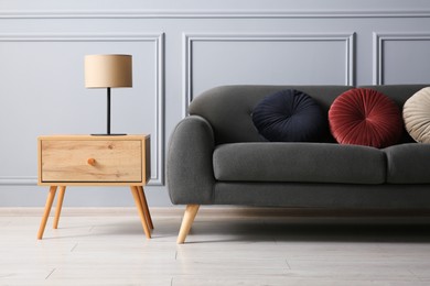 Photo of Stylish sofa with cushions and lamp on side table near grey wall