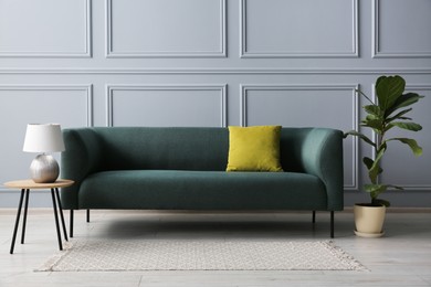 Photo of Stylish sofa with cushion, green plant and lamp on side table near grey wall