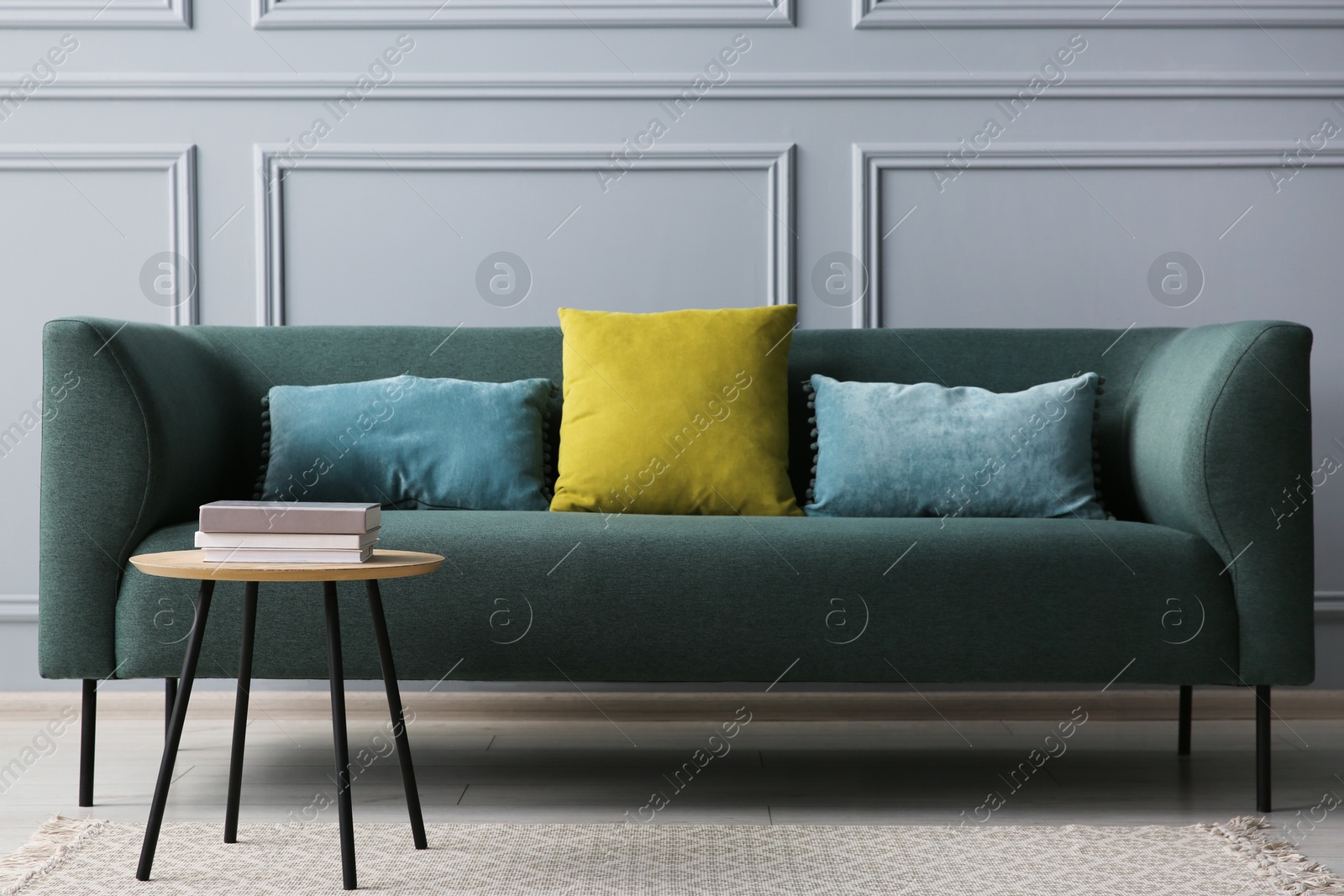 Photo of Stylish sofa with cushions and books on side table near grey wall