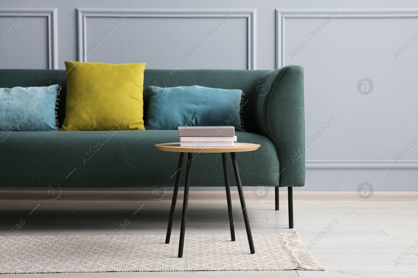 Photo of Stylish sofa with cushions and books on side table near grey wall