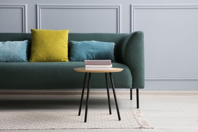 Photo of Stylish sofa with cushions and books on side table near grey wall