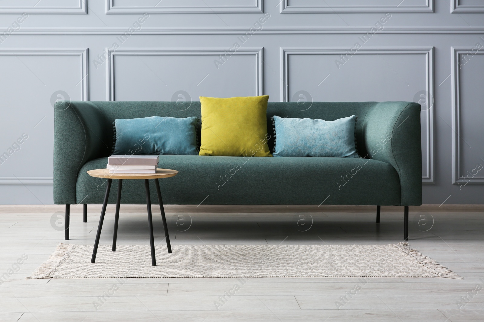 Photo of Stylish sofa with cushions and books on side table near grey wall