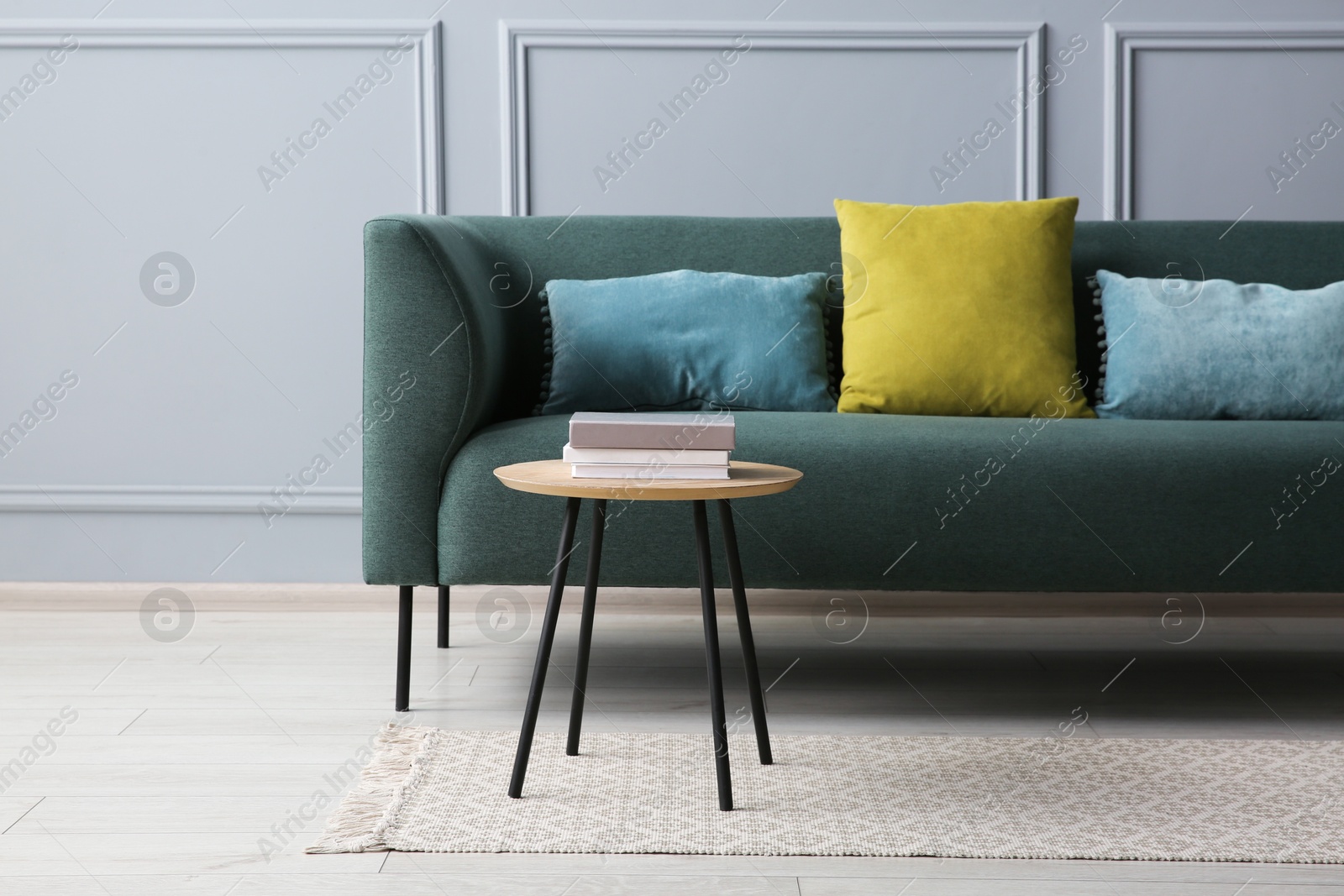 Photo of Stylish sofa with cushions and books on side table near grey wall