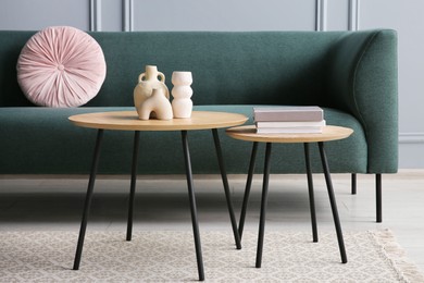 Photo of Stylish sofa with cushion, books and decor elements on nesting tables in room