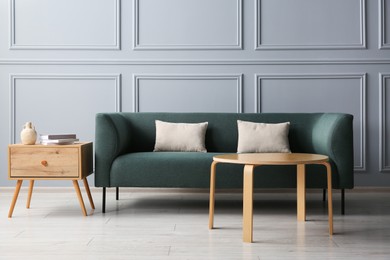 Photo of Stylish sofa with cushions, books and decor elements on side tables in room