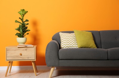 Photo of Stylish sofa with cushions, plant and books on side table near orange wall