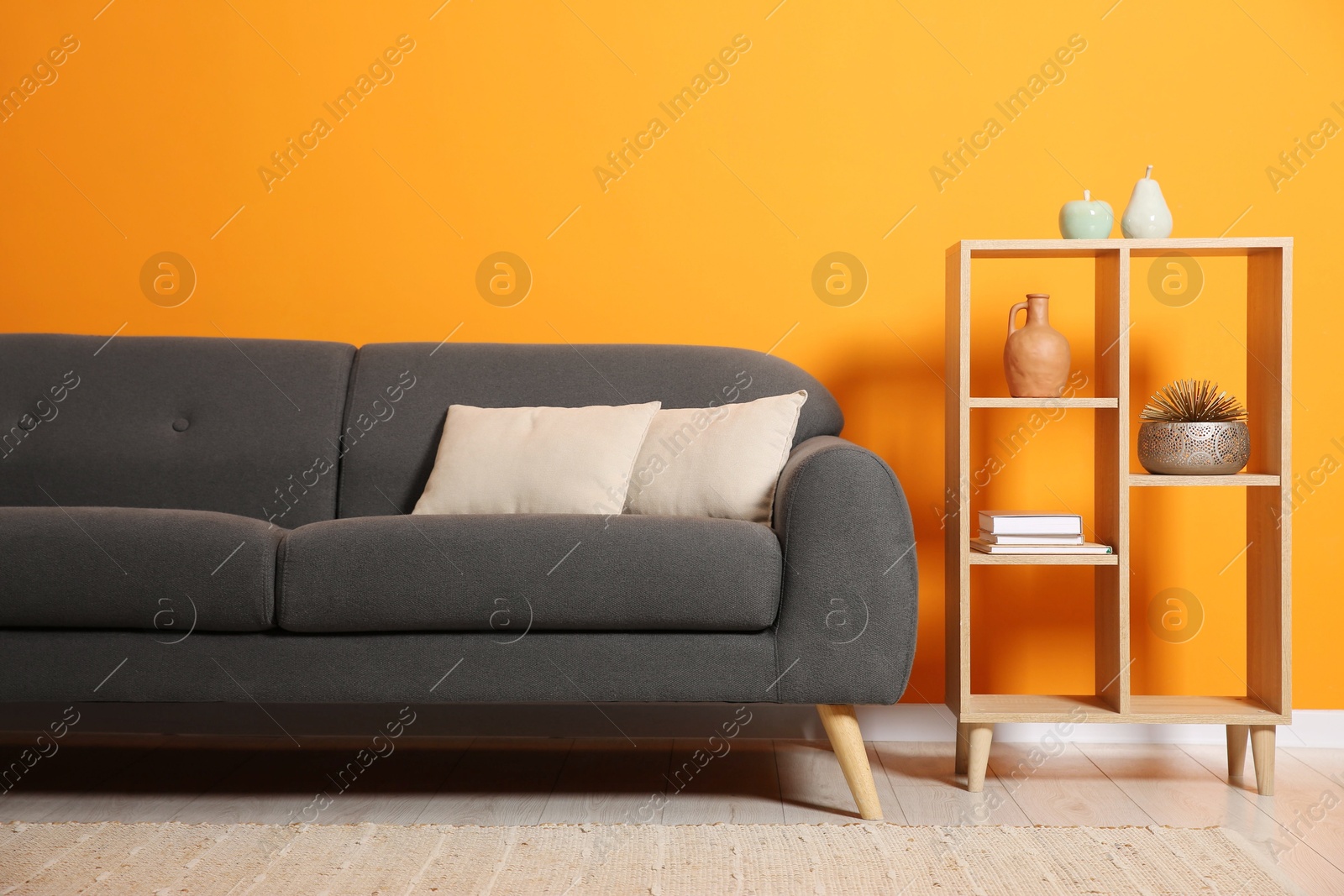 Photo of Stylish sofa with cushions and decor elements near orange wall