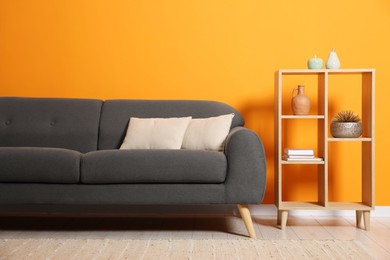 Photo of Stylish sofa with cushions and decor elements near orange wall