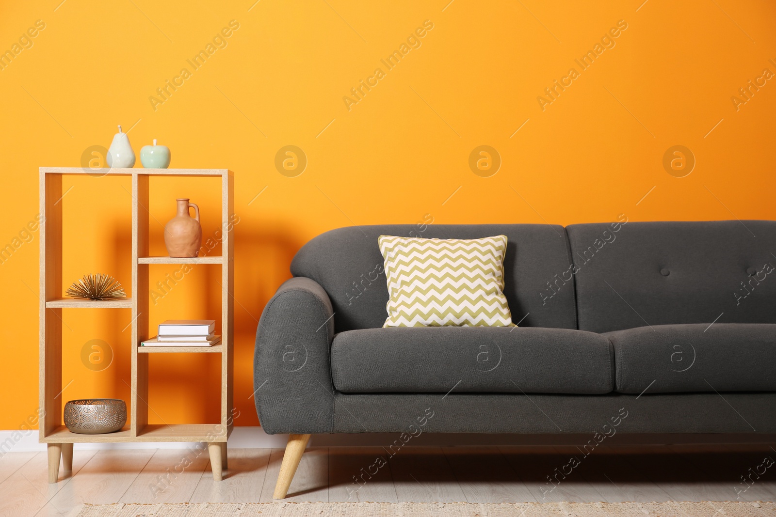 Photo of Stylish sofa with cushion and decor elements near orange wall