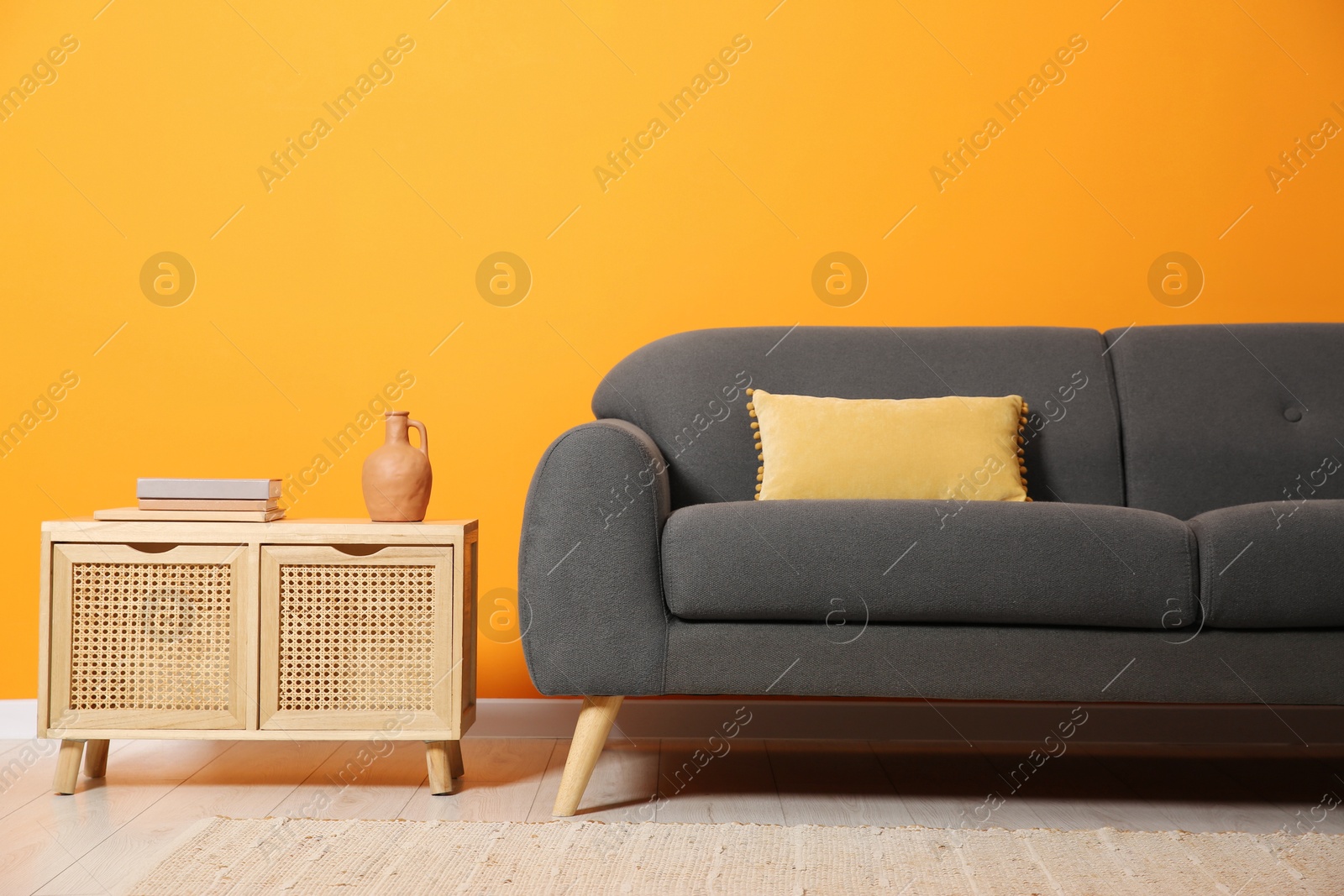 Photo of Stylish sofa with cushion and books on side table near orange wall