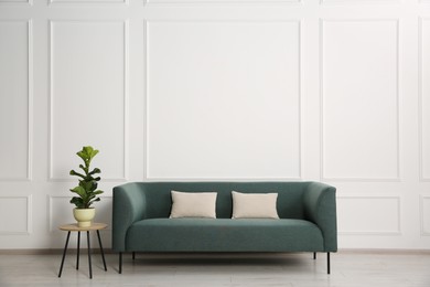 Photo of Stylish sofa with cushions and plant on side table near white wall