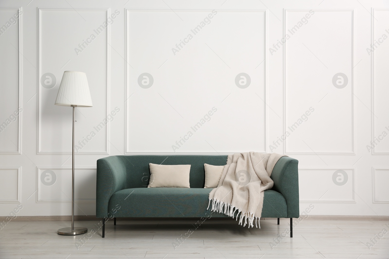 Photo of Stylish sofa with cushions, blanket and floor lamp near white wall