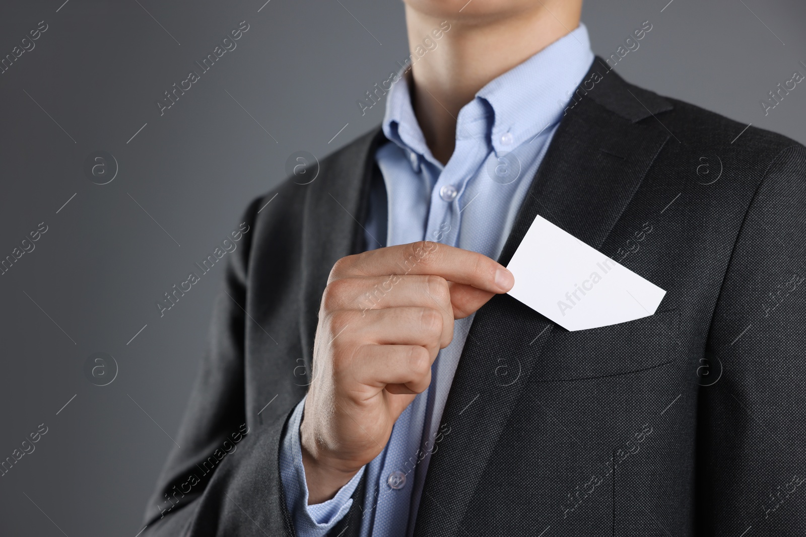 Photo of Man taking blank business card from pocket of his jacket on grey background, closeup. Mockup for design