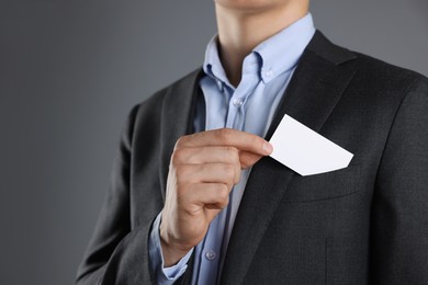 Man taking blank business card from pocket of his jacket on grey background, closeup. Mockup for design