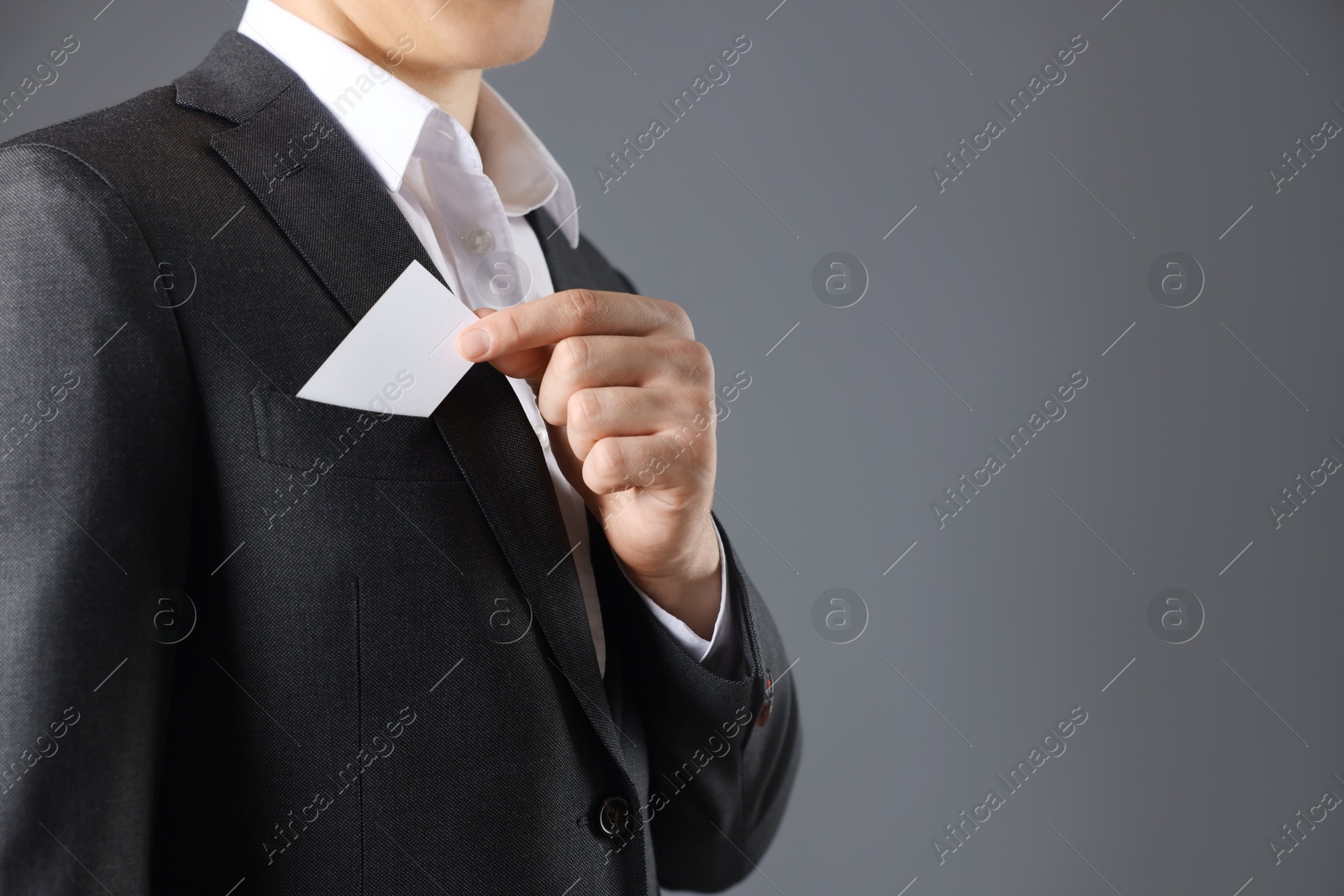 Photo of Man taking blank business card from pocket of his jacket on grey background, closeup. Mockup for design