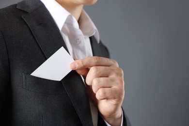 Photo of Man taking blank business card from pocket of his jacket on grey background, closeup. Mockup for design