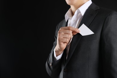 Photo of Man taking blank business card from pocket of his jacket on black background, closeup. Mockup for design